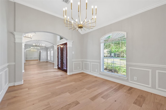 unfurnished dining area with decorative columns, light hardwood / wood-style floors, a notable chandelier, and ornamental molding