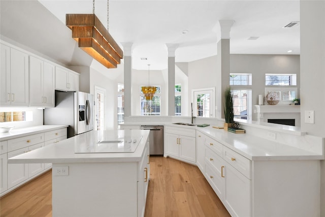 kitchen with kitchen peninsula, appliances with stainless steel finishes, decorative light fixtures, a center island, and light hardwood / wood-style floors