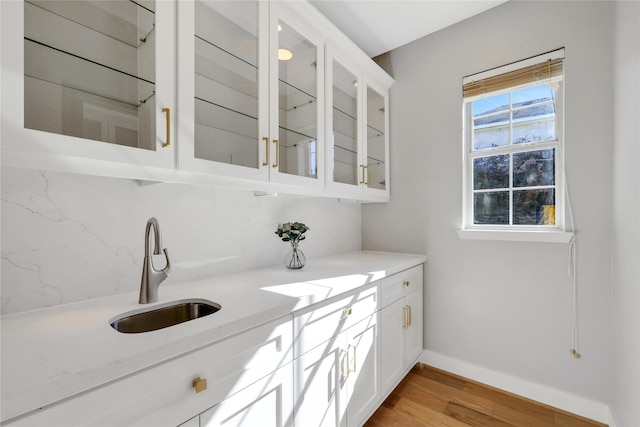 bar with white cabinets, light stone counters, sink, and light hardwood / wood-style flooring