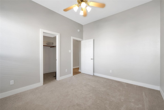 unfurnished bedroom featuring light carpet, a closet, a spacious closet, and ceiling fan