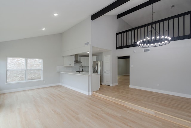 unfurnished living room with beam ceiling, light hardwood / wood-style floors, high vaulted ceiling, and sink