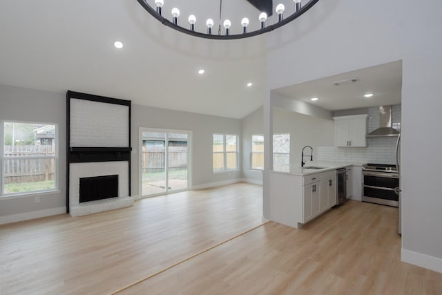 kitchen featuring a healthy amount of sunlight, stainless steel appliances, white cabinetry, and wall chimney exhaust hood