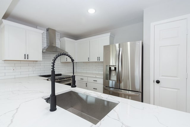 kitchen with decorative backsplash, appliances with stainless steel finishes, light stone countertops, wall chimney range hood, and white cabinetry