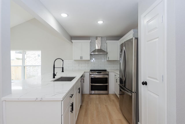 kitchen featuring sink, wall chimney exhaust hood, appliances with stainless steel finishes, light stone counters, and white cabinetry