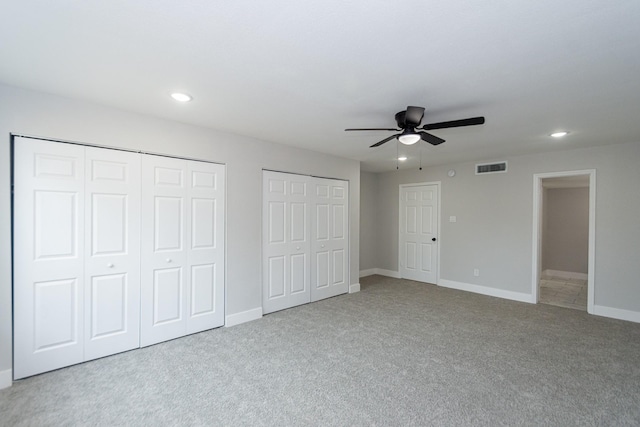 unfurnished bedroom featuring light carpet, ceiling fan, and multiple closets