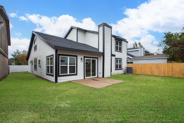 rear view of house with central AC unit and a lawn