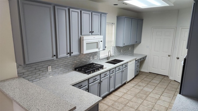 kitchen featuring sink, tasteful backsplash, light stone counters, white appliances, and gray cabinets