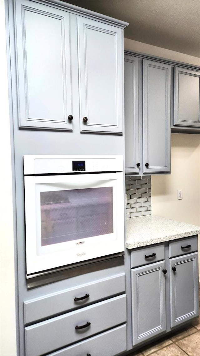 kitchen with backsplash, gray cabinets, oven, and light tile patterned floors