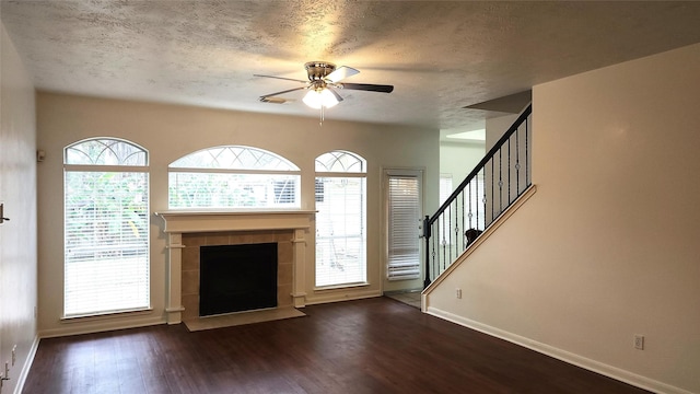 unfurnished living room featuring a textured ceiling, dark hardwood / wood-style floors, ceiling fan, and a tiled fireplace