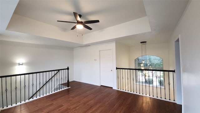 spare room featuring a tray ceiling, ceiling fan with notable chandelier, and dark hardwood / wood-style floors