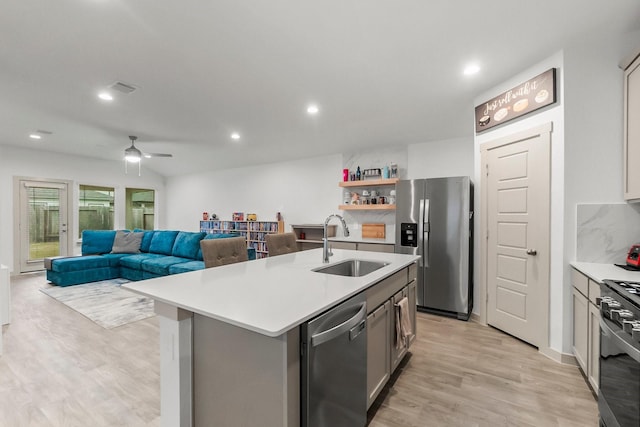 kitchen with appliances with stainless steel finishes, ceiling fan, a kitchen island with sink, sink, and light hardwood / wood-style flooring