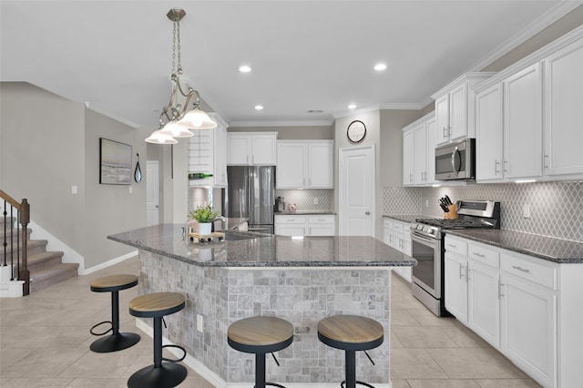 kitchen featuring backsplash, white cabinets, ornamental molding, an island with sink, and appliances with stainless steel finishes