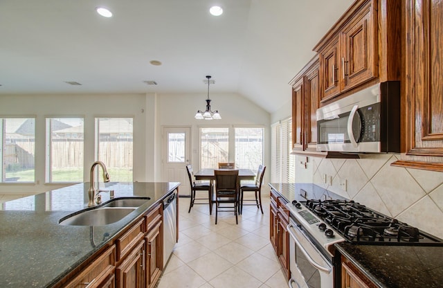 kitchen with sink, stainless steel appliances, dark stone counters, pendant lighting, and a chandelier