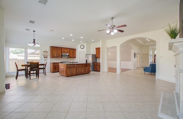 kitchen featuring ceiling fan with notable chandelier, stainless steel appliances, a kitchen island with sink, light tile patterned floors, and hanging light fixtures