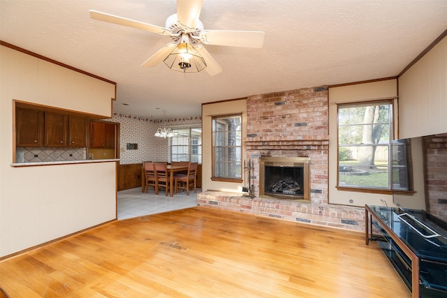 unfurnished living room featuring ceiling fan, light hardwood / wood-style floors, a textured ceiling, and a brick fireplace