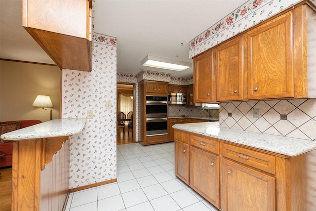 kitchen featuring light tile patterned floors, backsplash, stainless steel appliances, and light stone counters