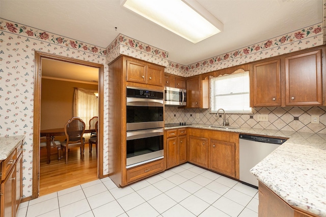 kitchen with light stone countertops, sink, stainless steel appliances, tasteful backsplash, and light hardwood / wood-style floors