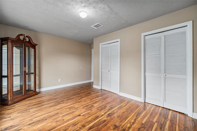 unfurnished bedroom featuring a textured ceiling, light hardwood / wood-style flooring, and multiple closets