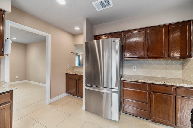 kitchen with tasteful backsplash, stainless steel fridge, light tile patterned floors, and light stone countertops