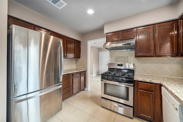 kitchen with appliances with stainless steel finishes, backsplash, extractor fan, and light stone counters