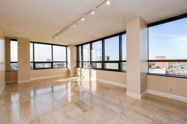 empty room with expansive windows, plenty of natural light, rail lighting, and a textured ceiling