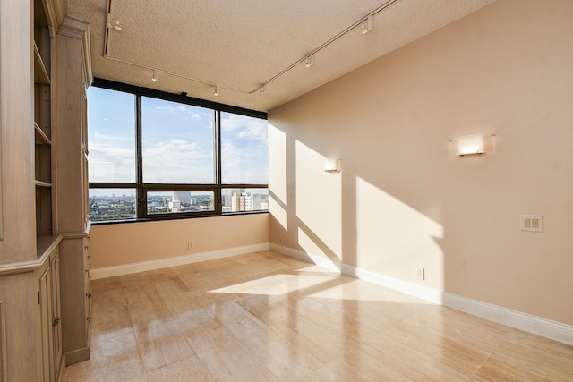 spare room with light wood-type flooring, a textured ceiling, track lighting, and plenty of natural light