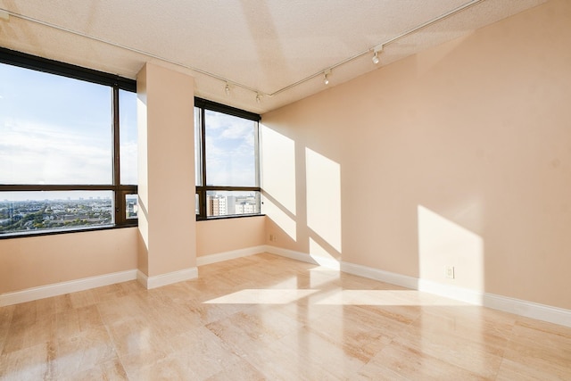 empty room featuring track lighting, a textured ceiling, and light hardwood / wood-style flooring