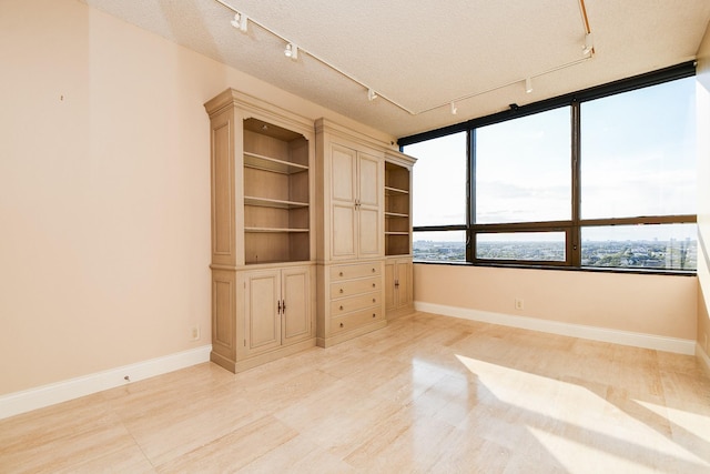 empty room with light wood-type flooring, a textured ceiling, and track lighting