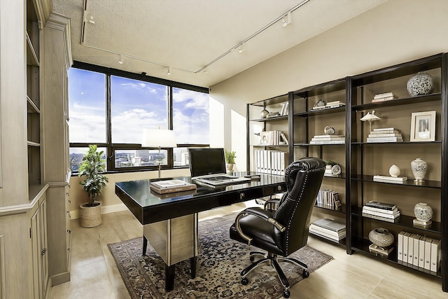 office space with a textured ceiling, rail lighting, light hardwood / wood-style flooring, and a wall of windows