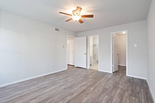 unfurnished bedroom featuring a walk in closet, connected bathroom, light hardwood / wood-style flooring, and ceiling fan