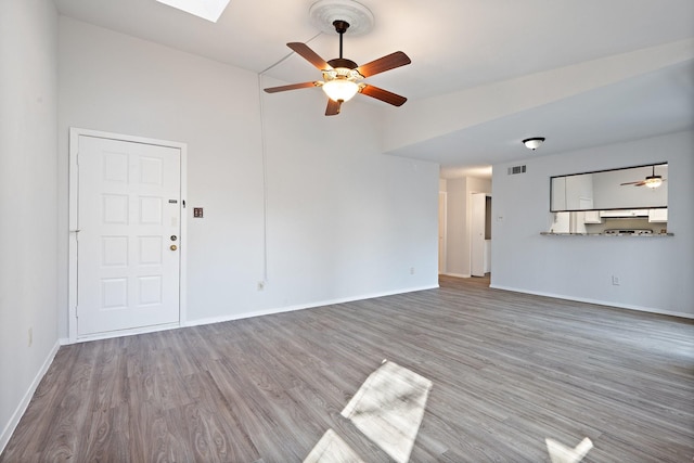 unfurnished living room featuring a skylight, ceiling fan, and wood-type flooring