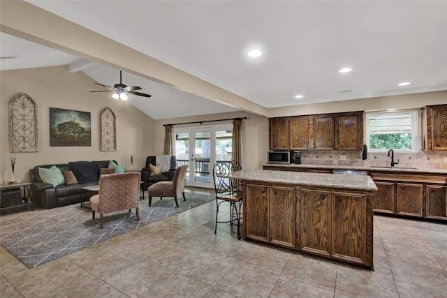 kitchen featuring sink, backsplash, a center island, lofted ceiling with beams, and a kitchen bar