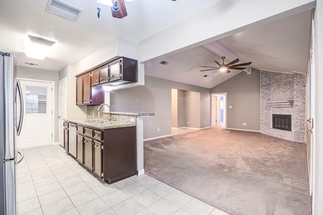 kitchen with lofted ceiling with beams, a brick fireplace, light colored carpet, dark brown cabinetry, and stainless steel refrigerator