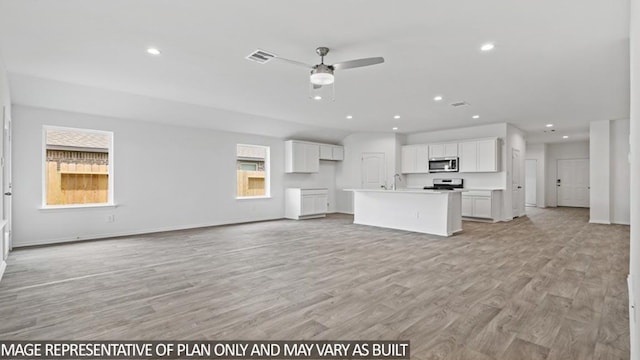 unfurnished living room featuring ceiling fan, a healthy amount of sunlight, light wood-type flooring, and sink