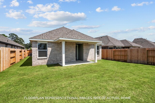 rear view of house featuring brick siding, roof with shingles, a lawn, a fenced backyard, and a patio area