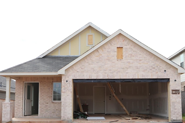 rear view of house featuring brick siding, a garage, and a shingled roof