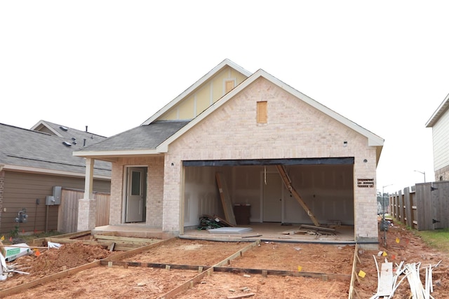 view of front of house with fence, an attached garage, a shingled roof, an outdoor structure, and brick siding