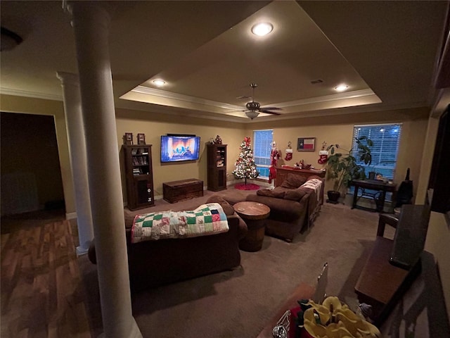 carpeted living room with decorative columns, a raised ceiling, ceiling fan, and crown molding