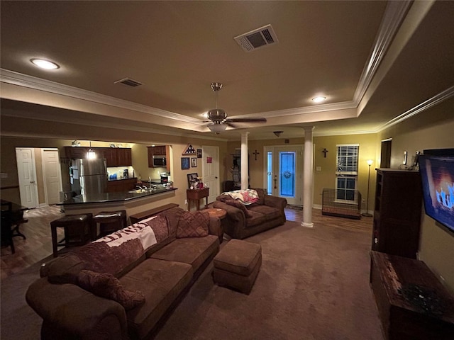 cinema room featuring ceiling fan, decorative columns, crown molding, a tray ceiling, and dark carpet