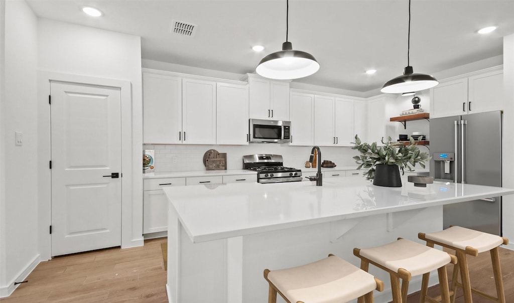 kitchen with stainless steel appliances, a center island with sink, white cabinets, and hanging light fixtures