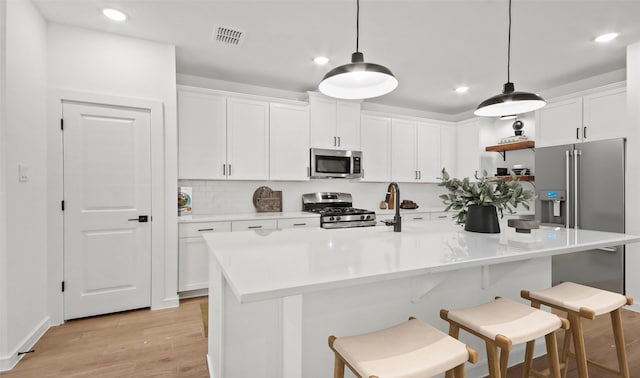 kitchen with stainless steel appliances, a center island with sink, white cabinets, and hanging light fixtures