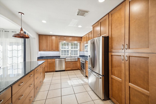 kitchen featuring appliances with stainless steel finishes, sink, light tile patterned floors, dark stone countertops, and hanging light fixtures