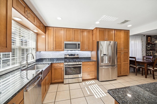 kitchen featuring backsplash, stainless steel appliances, sink, light tile patterned floors, and dark stone countertops