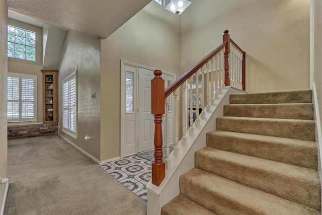 foyer featuring carpet flooring, a textured ceiling, and a towering ceiling