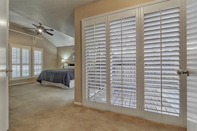 bedroom with ceiling fan, light colored carpet, lofted ceiling, and a textured ceiling