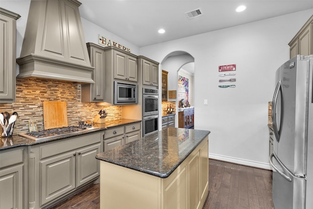 kitchen with appliances with stainless steel finishes, dark hardwood / wood-style flooring, custom exhaust hood, and dark stone countertops