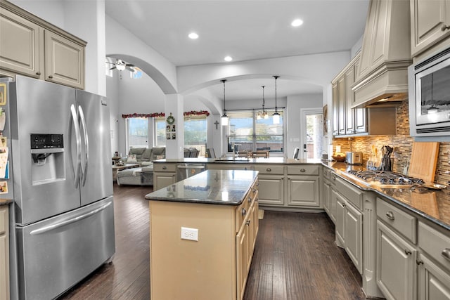 kitchen with ceiling fan with notable chandelier, stainless steel appliances, dark wood-type flooring, pendant lighting, and a kitchen island