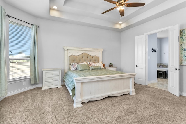 carpeted bedroom with ensuite bath, a raised ceiling, and ceiling fan