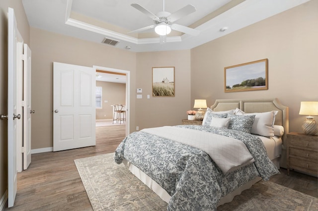 bedroom with ceiling fan, wood-type flooring, and a tray ceiling