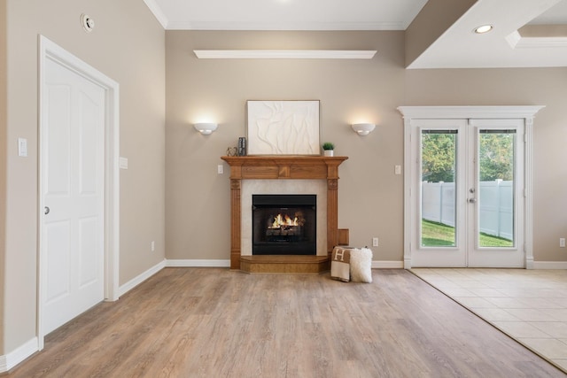 unfurnished living room with a tiled fireplace, light hardwood / wood-style flooring, french doors, and ornamental molding